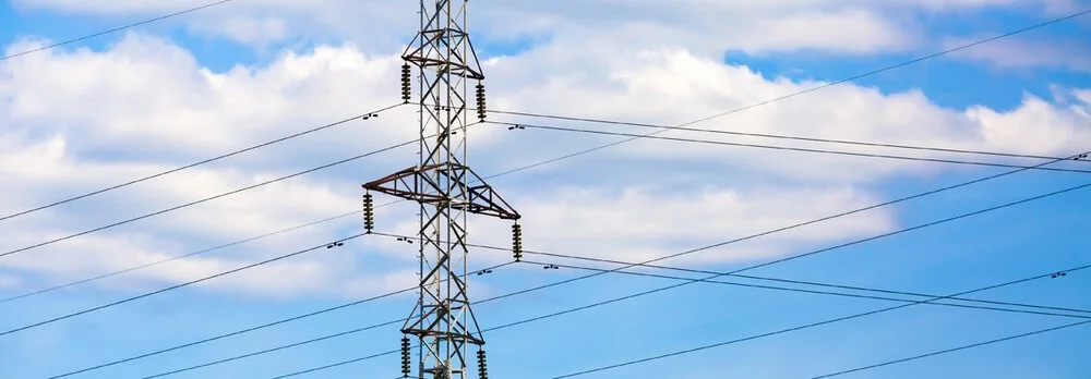 Close-up of an electrical transmission tower with power lines against a partly cloudy sky.