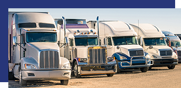 Row of parked semi-trucks and delivery vans on a dirt lot.