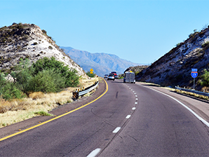 A scenic highway curving through rocky hills with vehicles traveling in both directions under a clear blue sky.