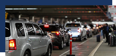 Line of cars and travelers at an airport terminal with luggage carts outside