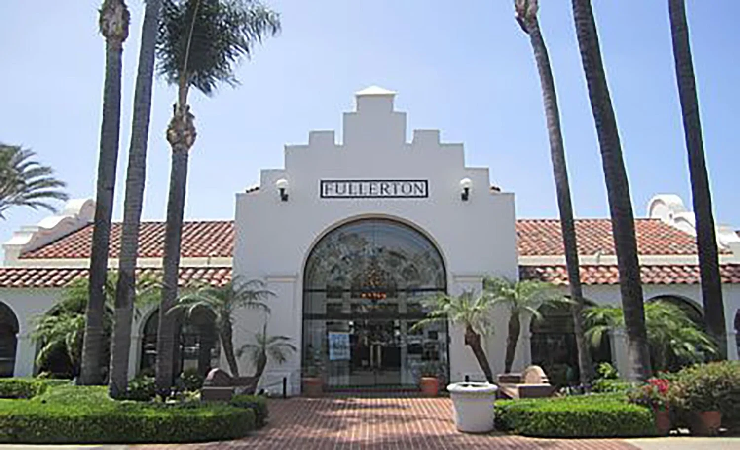 The Fullerton shopping center with a white facade, red-tiled roof, arched entrance, and tall palm trees in front.