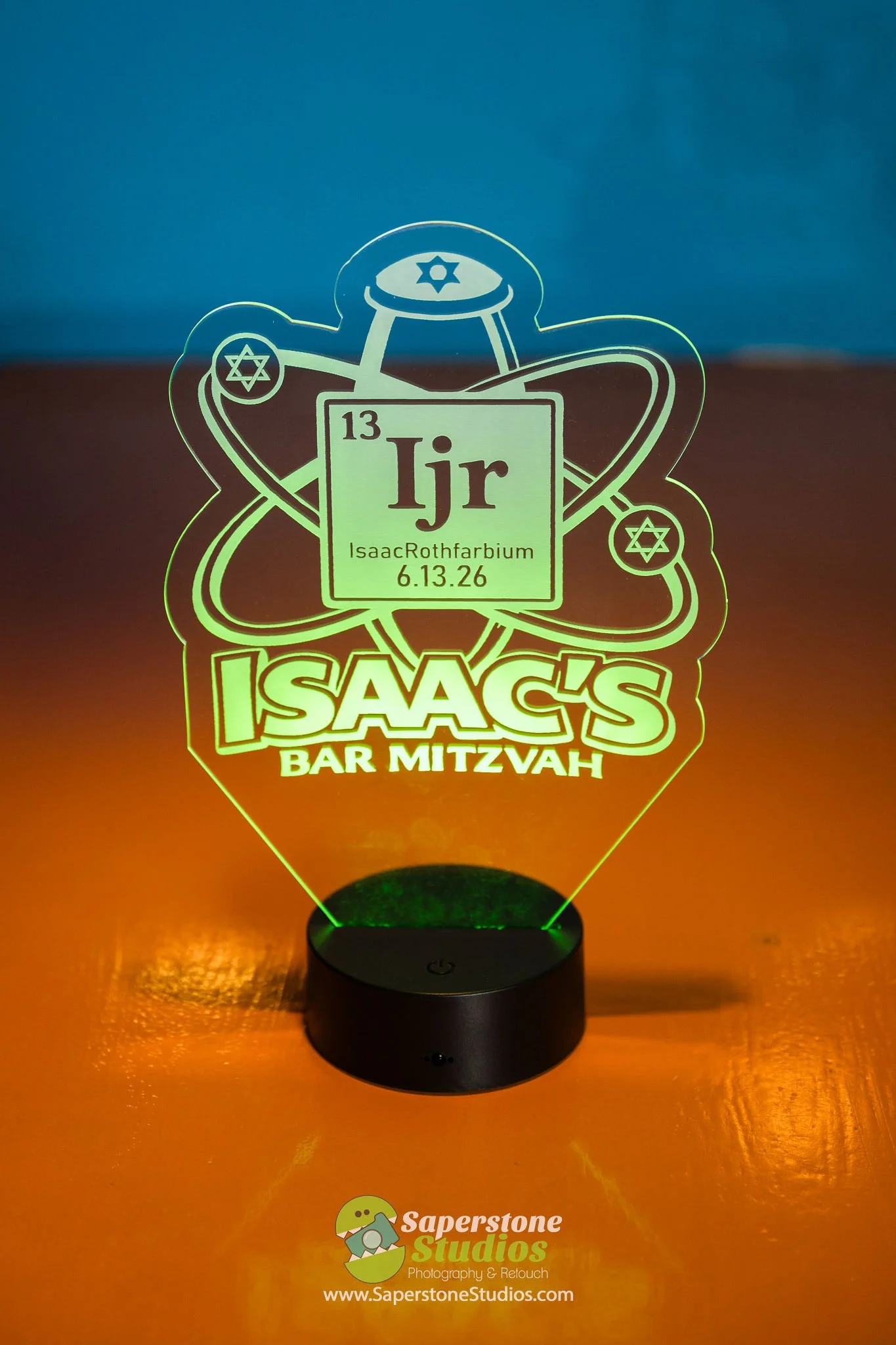 A decorative LED light featuring a representation of the chemical element lithium (Li) from the periodic table, with the abbreviation 'Ijr', the date 6.13.26, and the name Isaac Rothfarbium. The design includes atomic orbitals and Star of David symbo