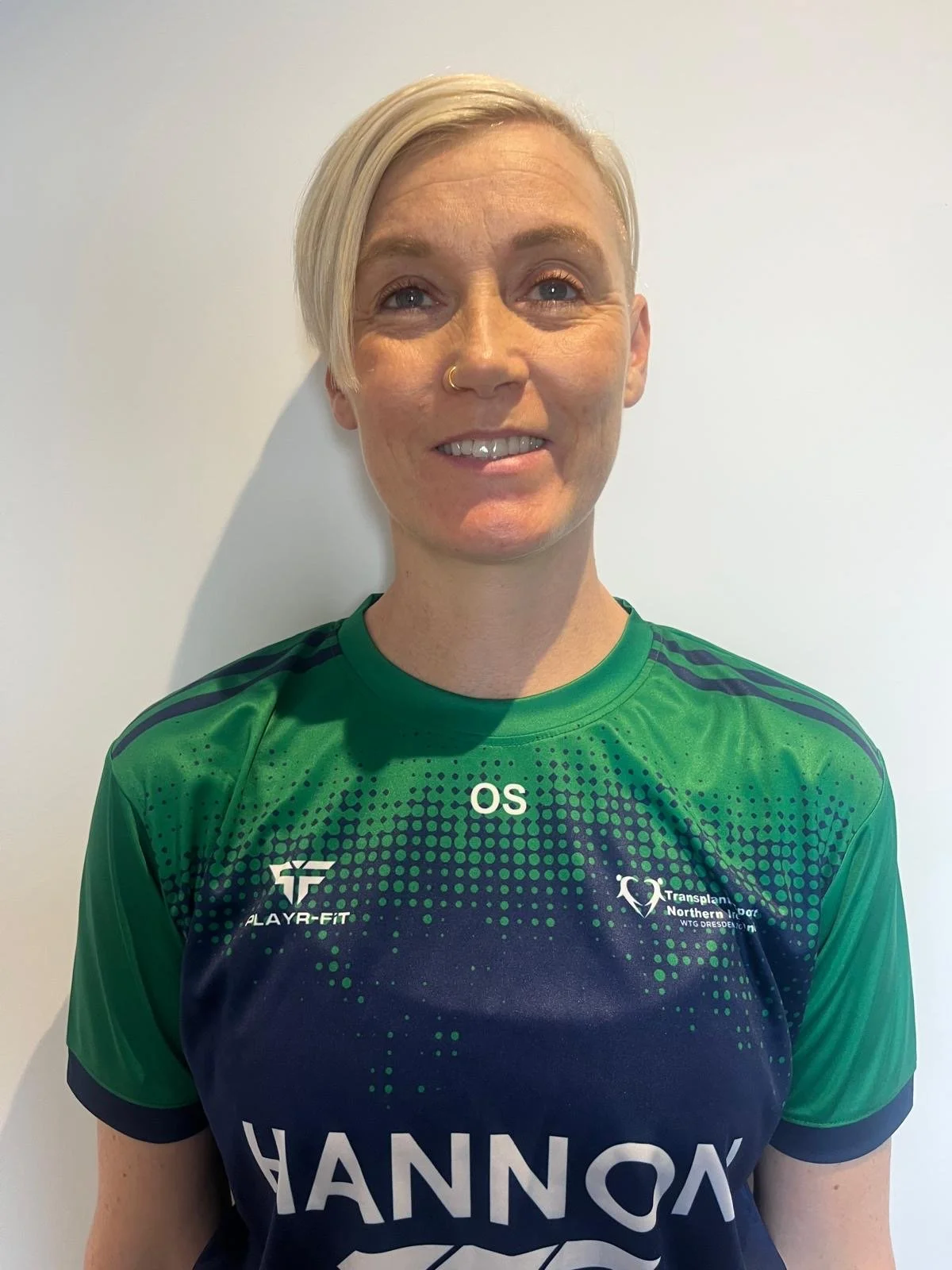 Woman wearing a green and navy athletic jersey standing against a plain white background, smiling at the camera.