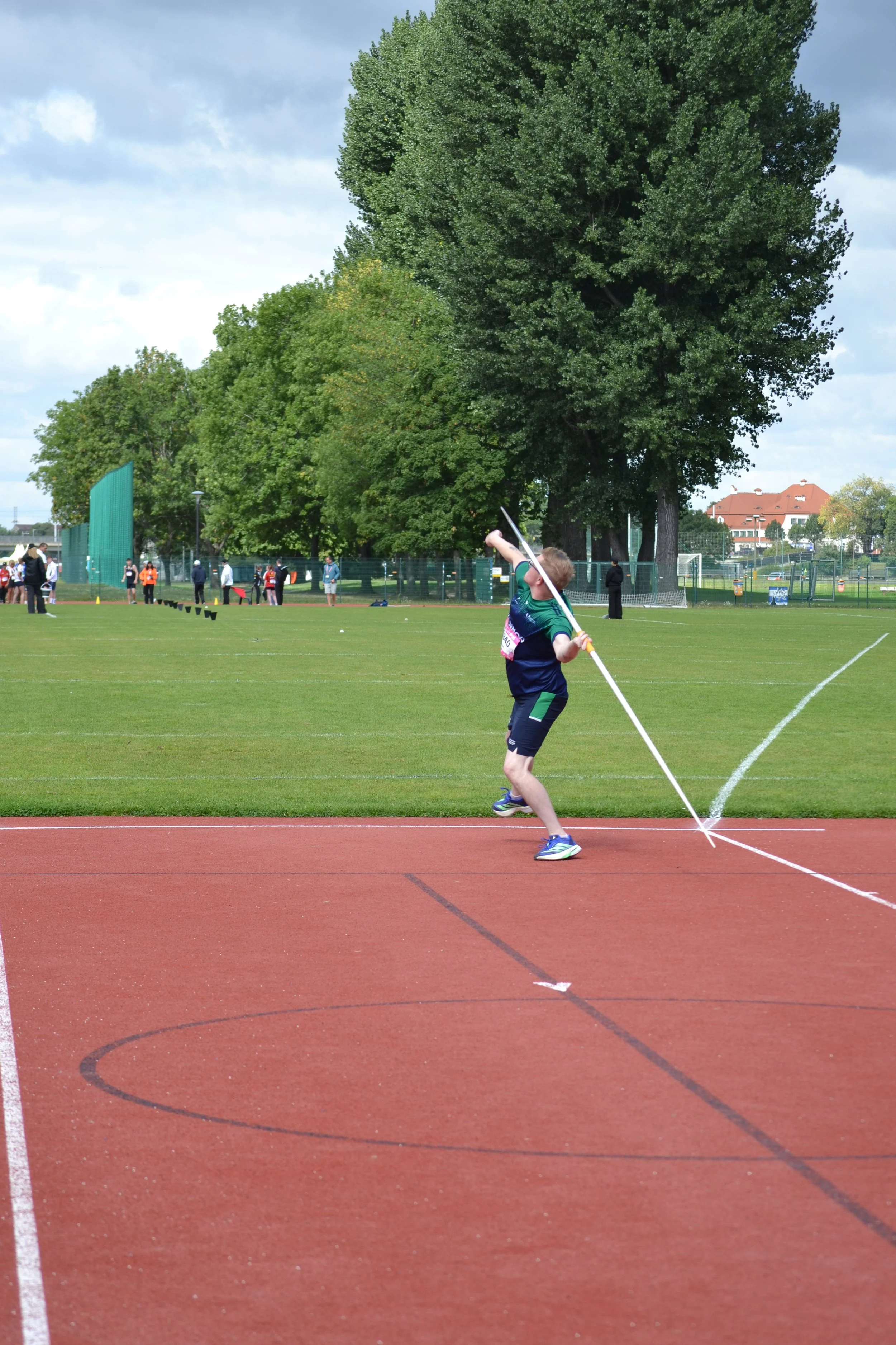 Young male athlete in green sportswear throwing a javelin on a running track during a sporting event
