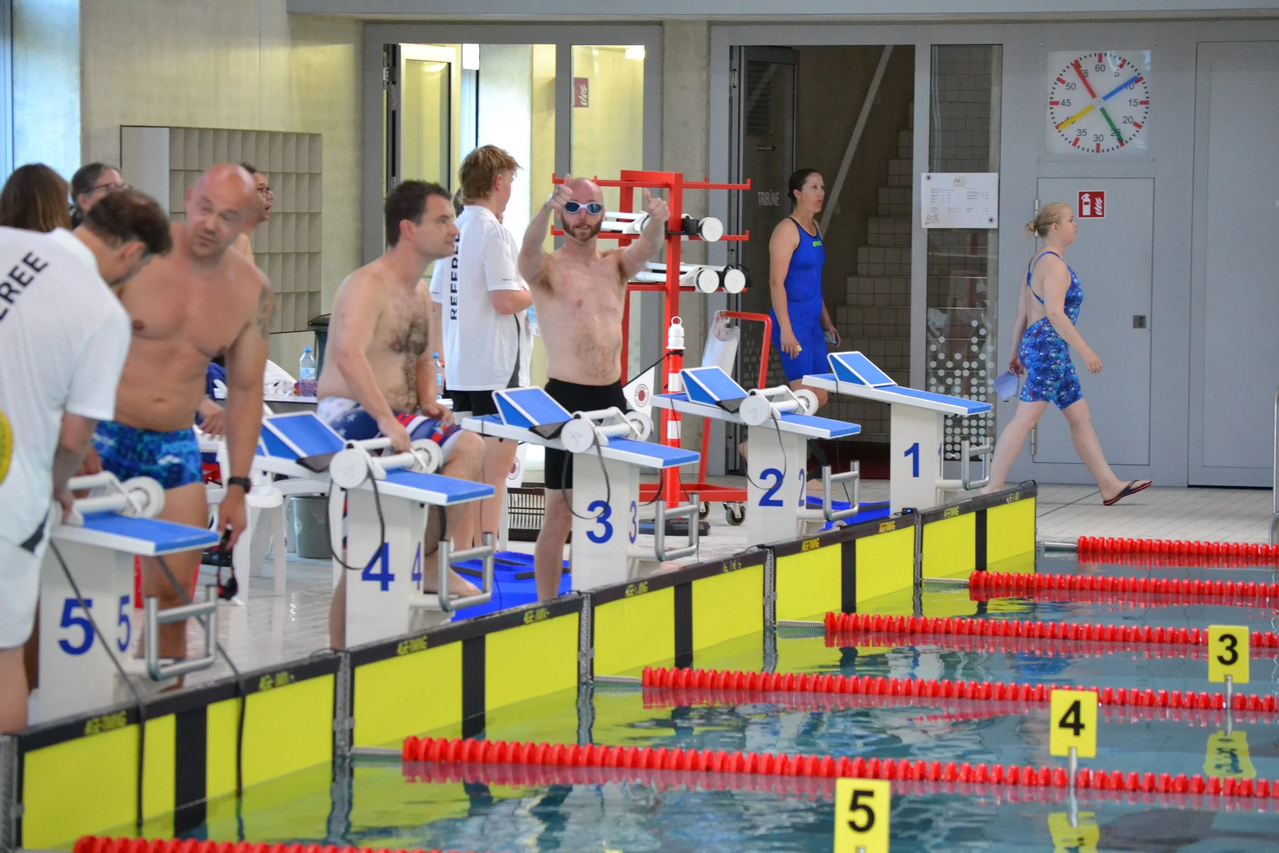 Swimmers standing at starting blocks ready for a race at an indoor swimming pool.