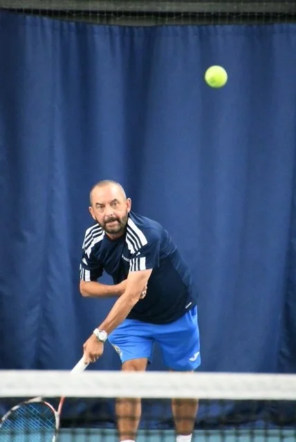 A man playing tennis indoors, preparing to hit a tennis ball over the net.