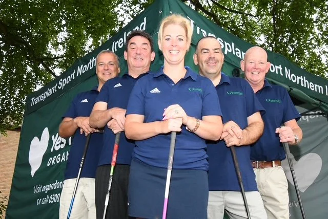 Five people in blue polo shirts standing in front of a green tent, holding golf clubs, smiling at the camera.