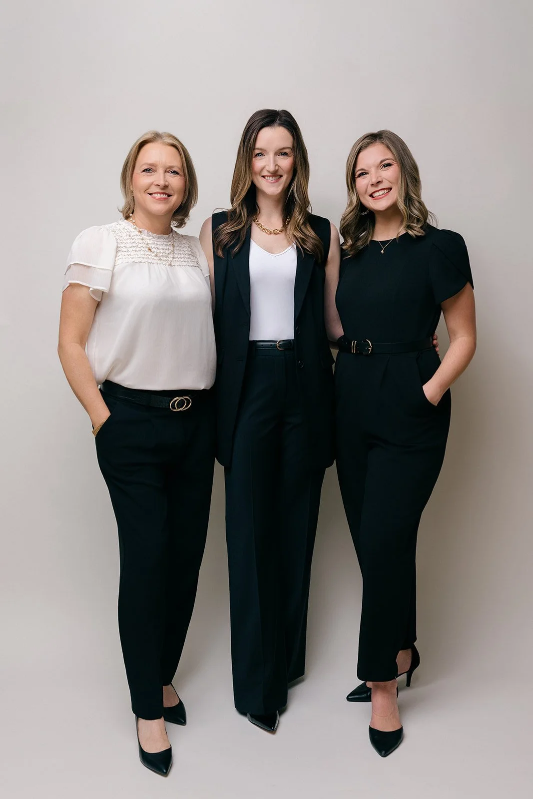 Three women in professional attire standing together against a plain white background.
