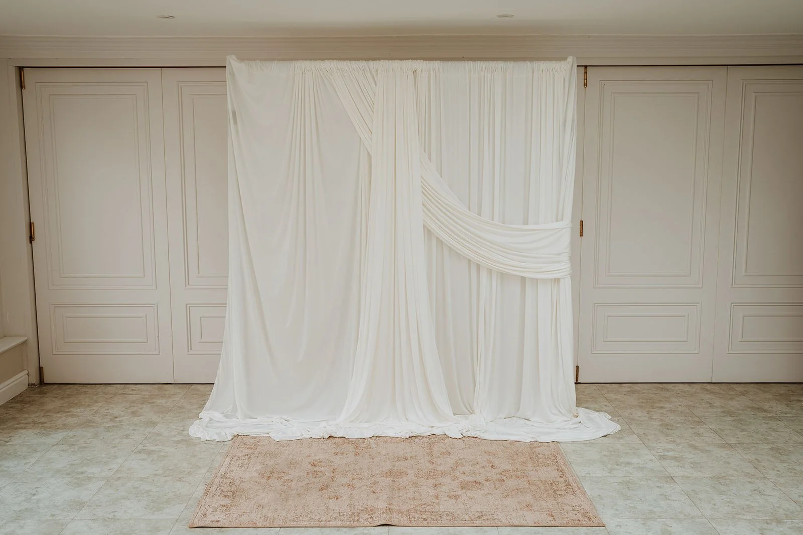 White draped fabric backdrop in a room with beige tiled floor, set against closet doors.