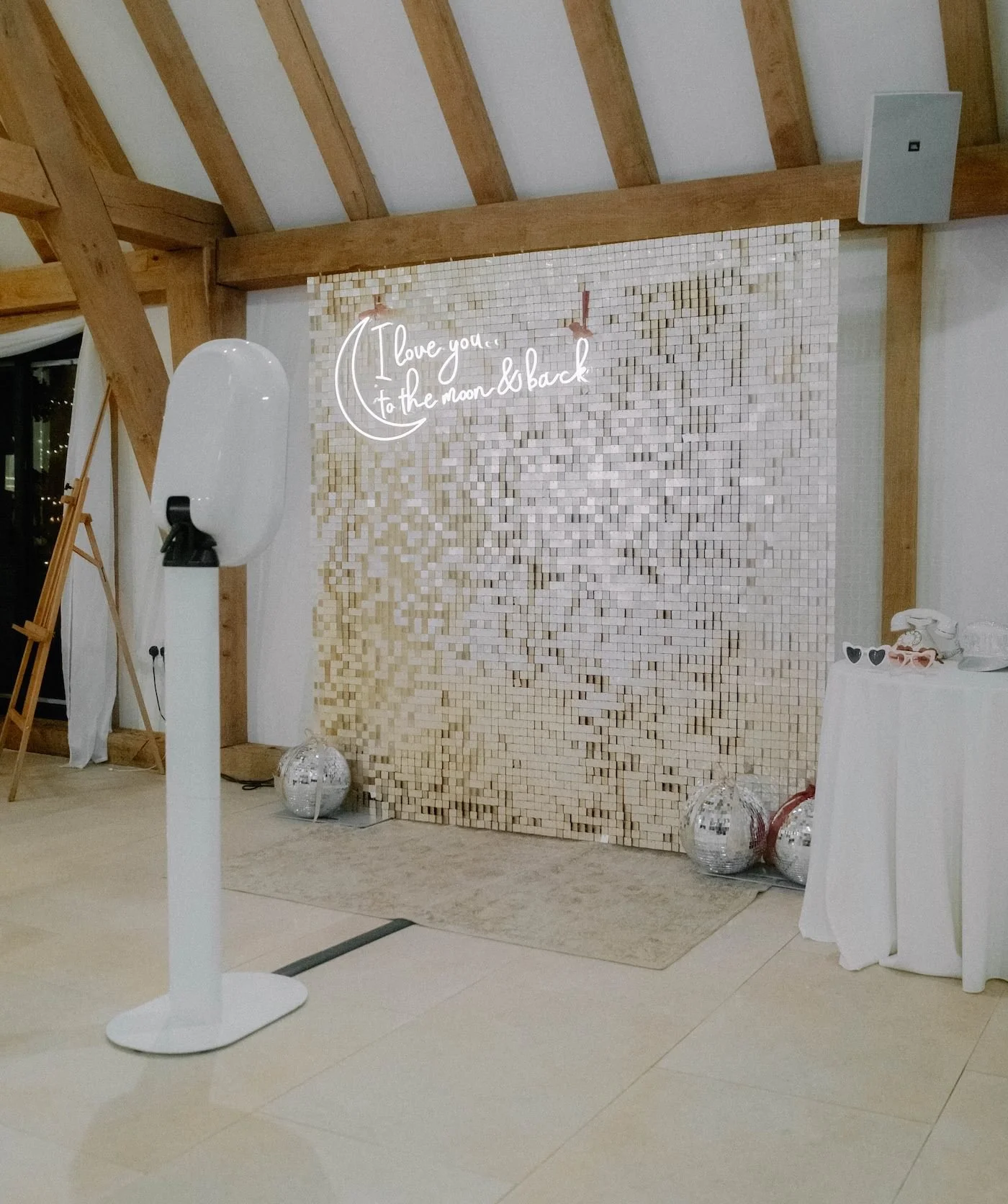 Decorative backdrop with a neon sign that says 'I love you to the moon & back,' surrounded by balloons and decorative objects in a modern indoor setting.
