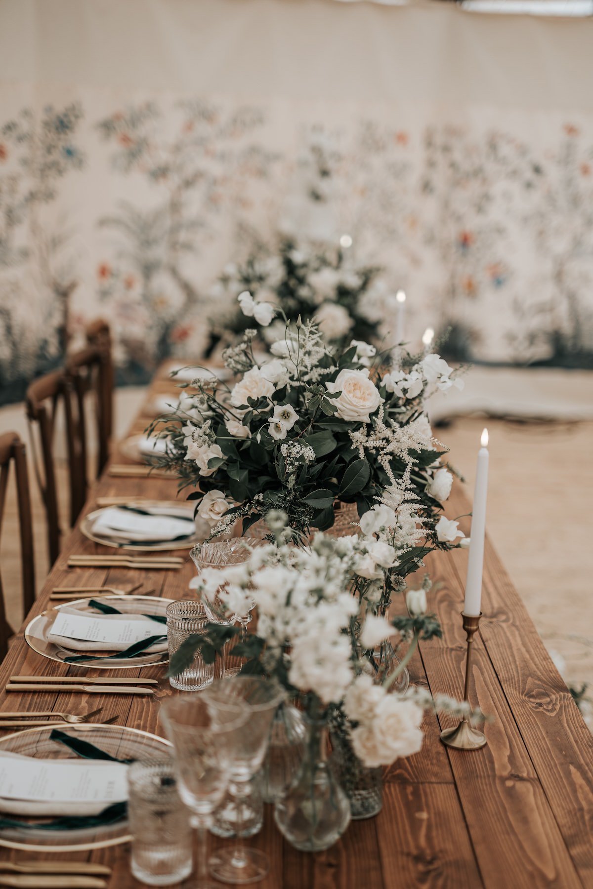 A decorated dining table with floral arrangements, candles, and place settings, set in a rustic style with a wooden table and chairs.