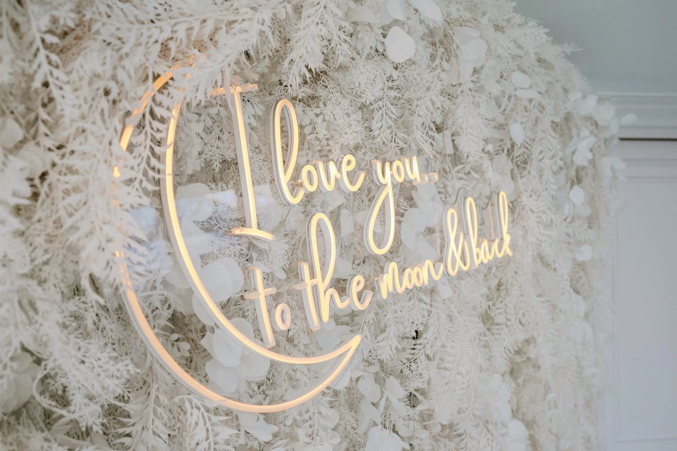 White floral wall with illuminated neon sign that reads "love you to the moon and back."