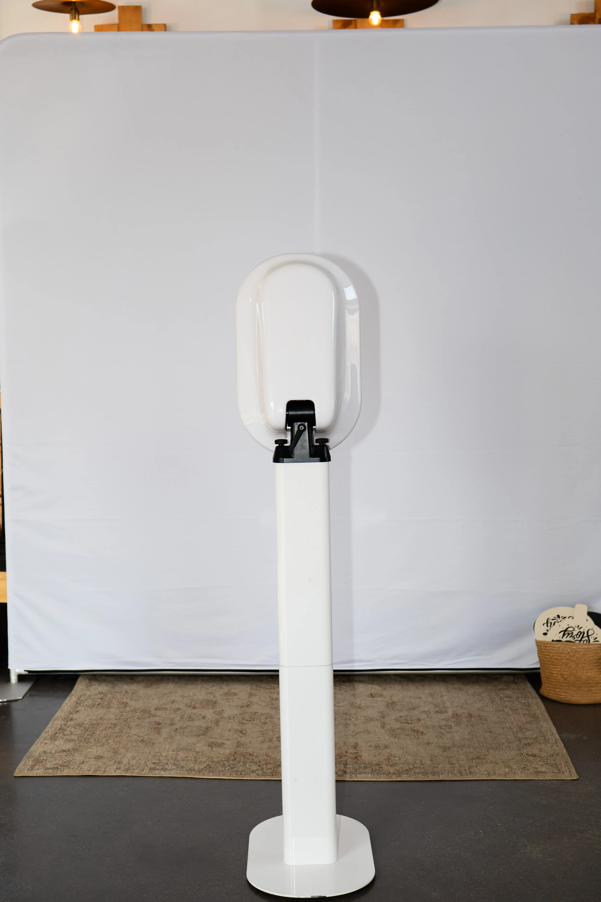 A photo booth in front of a white background with a beige rug underneath. Part of a basket is visible on the right side of the image.