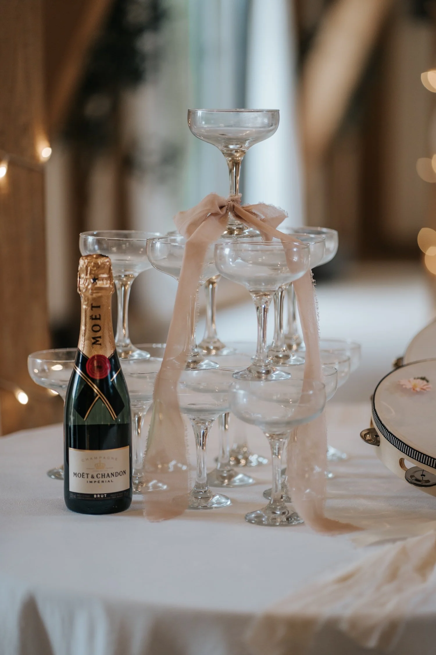 A pyramid of empty champagne glasses decorated with a pink ribbon, with a bottle of Moët & Chandon Champagne on a white tablecloth, set for celebration.