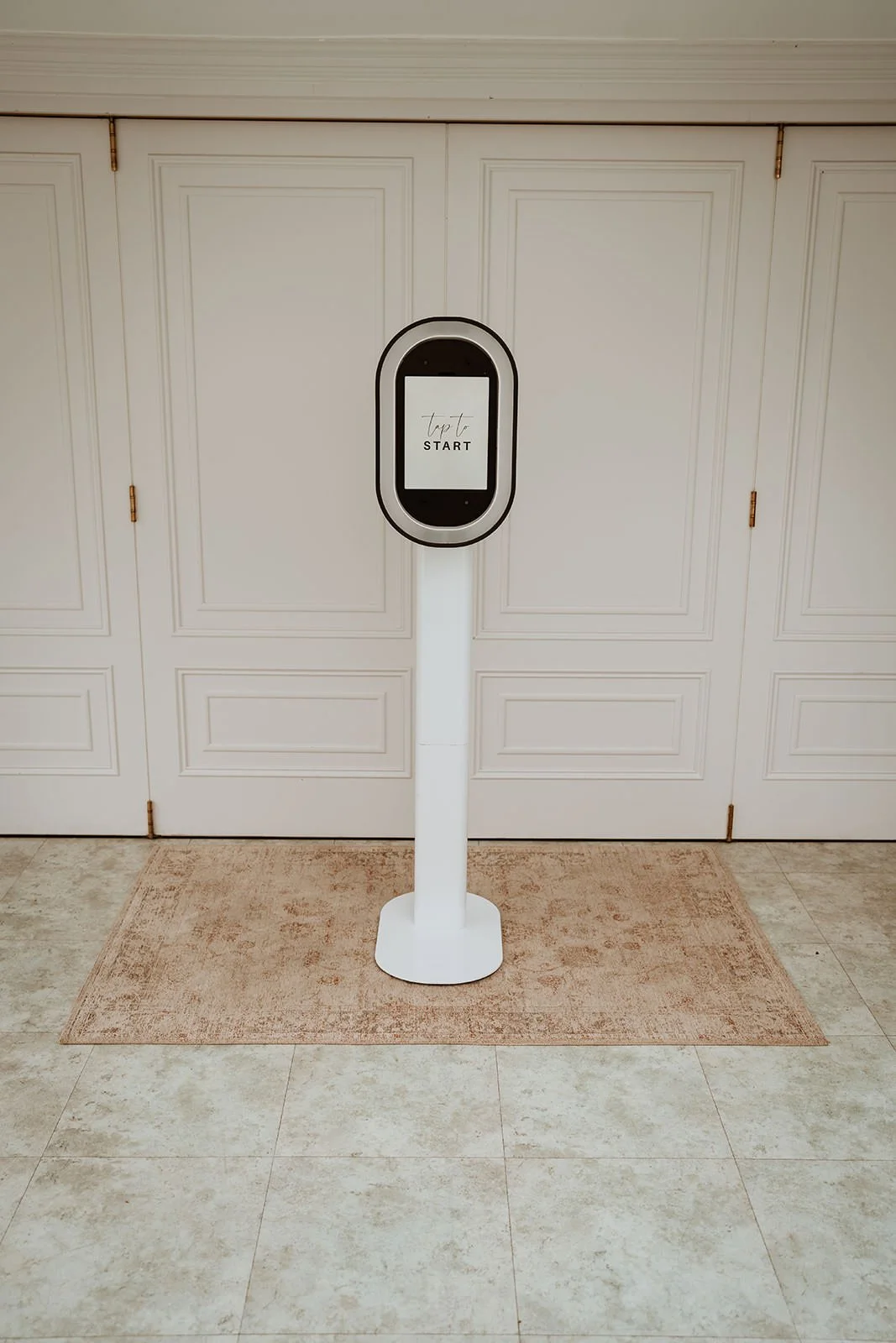 A photo booth  in front of white closet doors with a beige carpeted mat underneath.