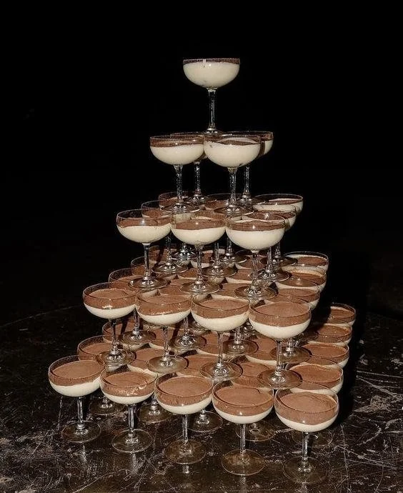 Stacked glasses of layered dessert, topped with cocoa powder, arranged in a pyramid shape.