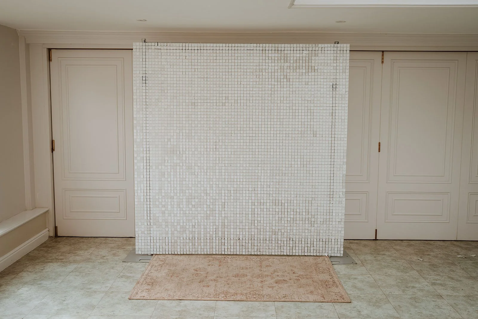 A white shimmer wall backdrop is positioned in front of a set of double closet doors in a room with light-colored walls and flooring.