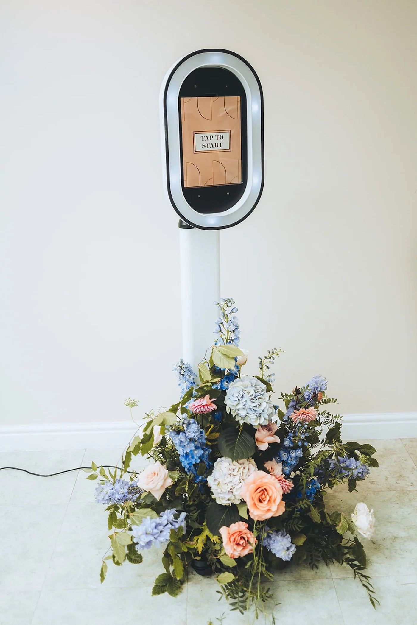 A flower arrangement with roses, hydrangeas, and greenery on the floor in front of a digital sports scoreboard that says "Tap to Start".