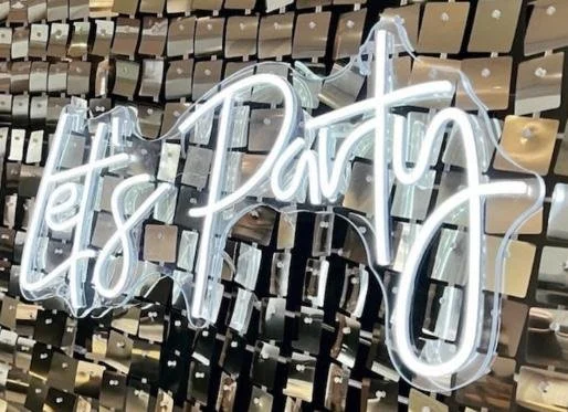 A neon sign reads '& lets party in cursive, mounted on a wall with a textured, mosaic pattern
