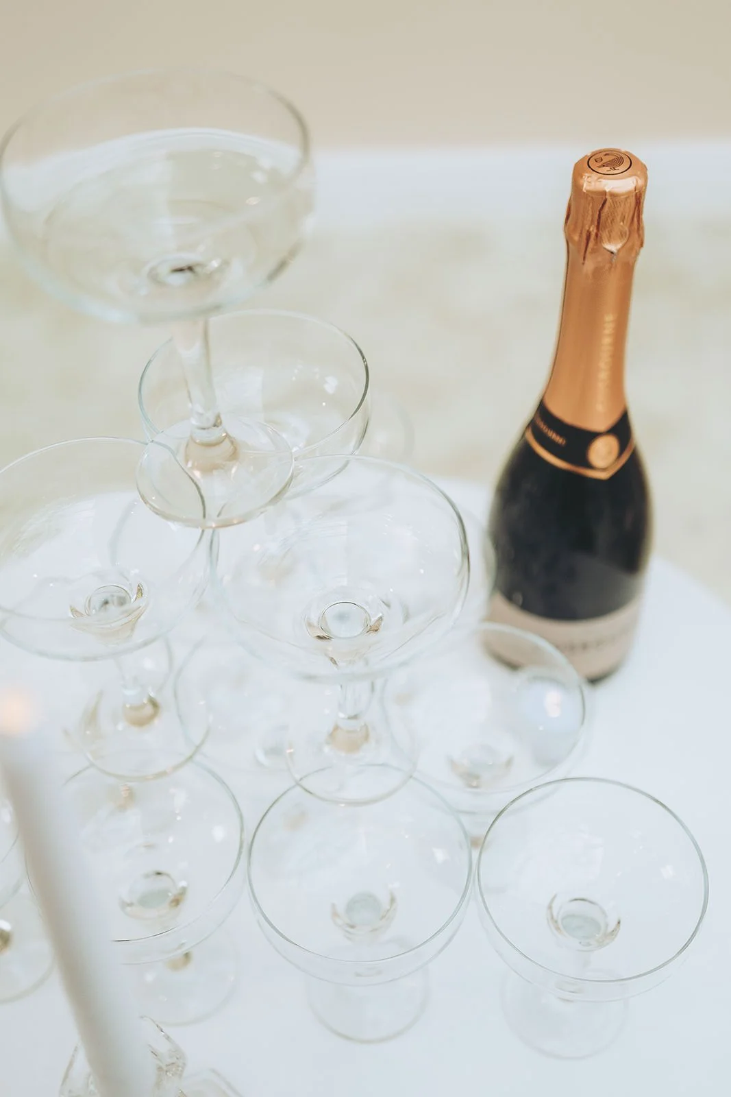 Empty champagne glasses arranged in a tower with a bottle of champagne on a white table.