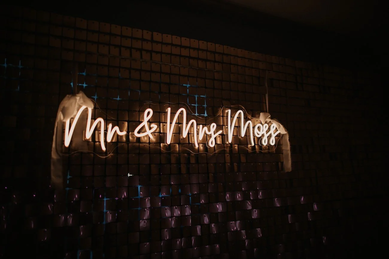 Neon sign reading 'Mr & Mrs Mogg' on a brick wall with some fabric decorations.