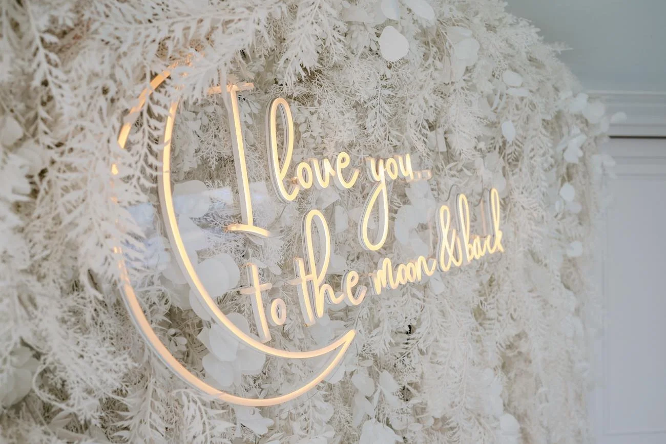 Decorative wall with white floral arrangement and illuminated sign that says 'I love you to the moon and back' in cursive script.