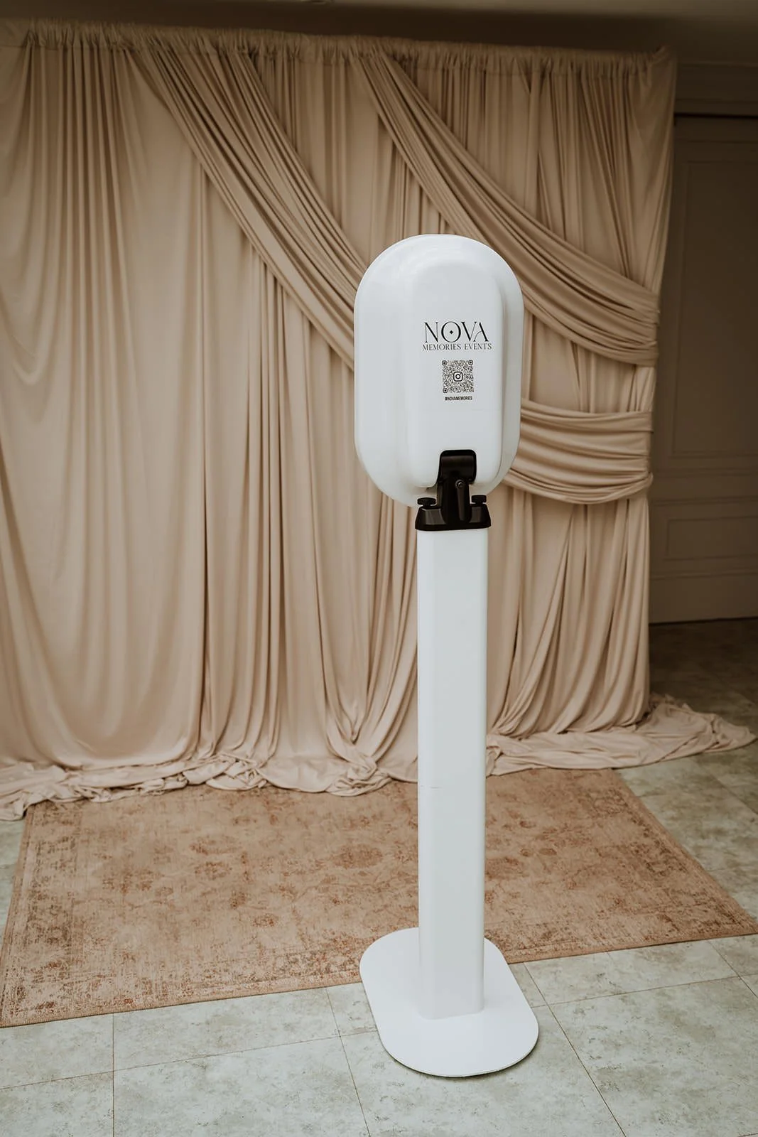 Photo Booth with a beige draped curtain backdrop and a pinkish rug on the floor.
