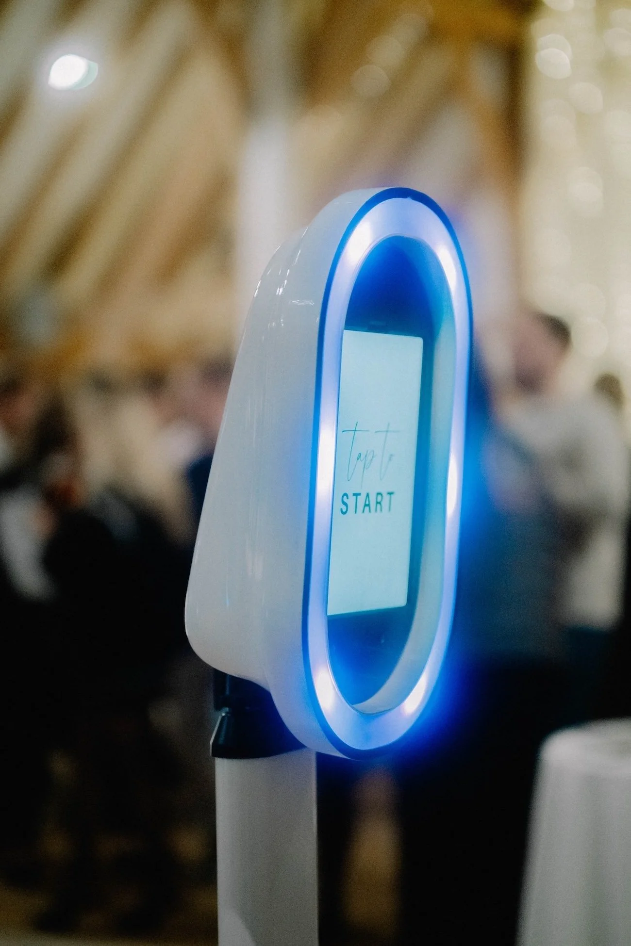 Close-up of a digital device with a glowing blue circular ring, displaying the word 'Tap to START' on its screen, against a blurred background.