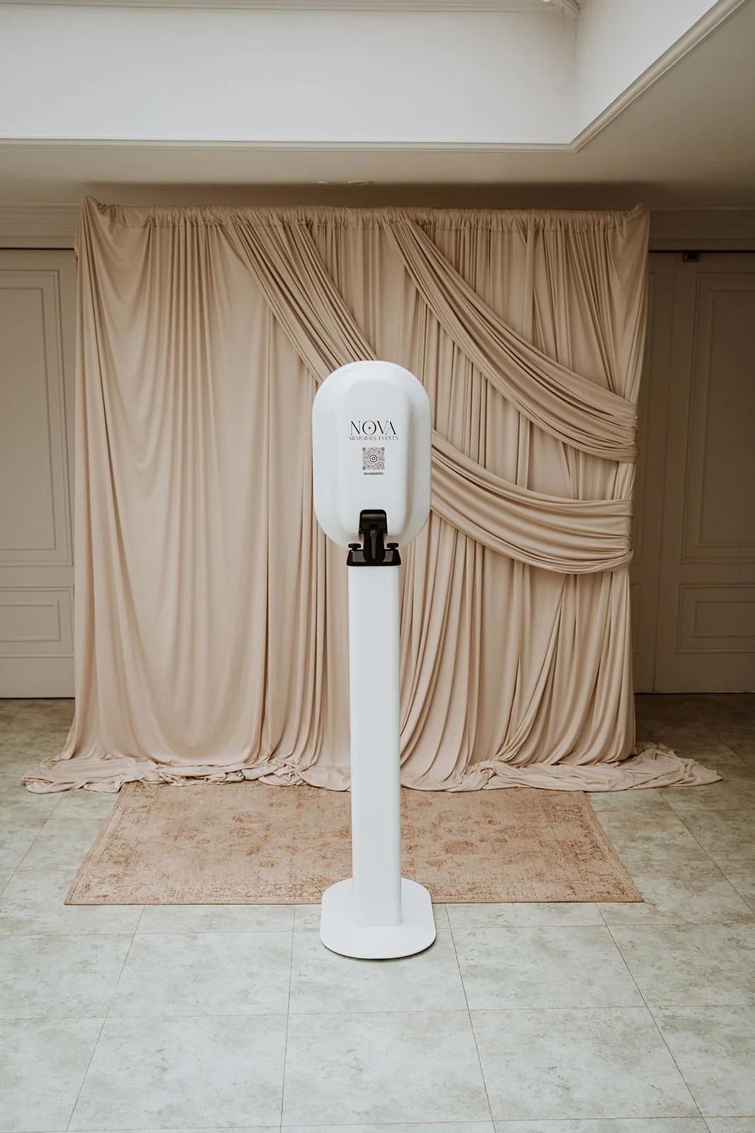A photo booth in front of beige draped curtains and a rug on a tile floor.