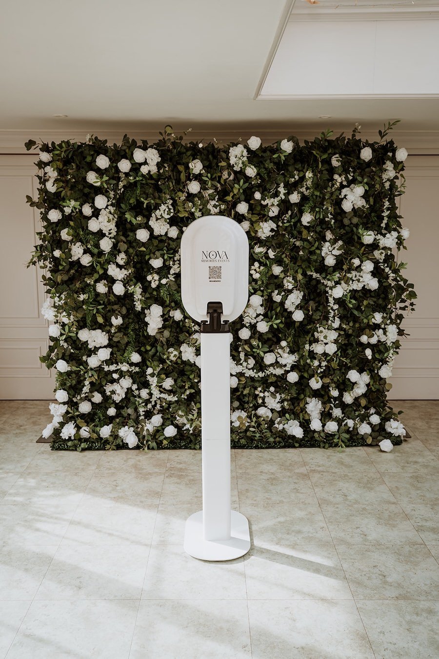 Photo Booth on a stand in front of a green and white floral backdrop in an indoor setting.