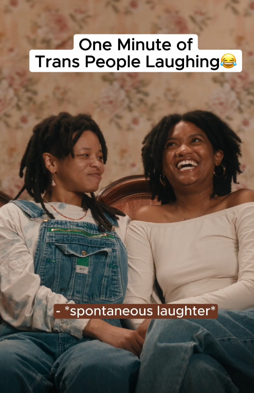 Loving trans couple sits on vintage couch with floral backdrop. Text reads, "One Minute of Trans People Laughing". Links to Instagram.