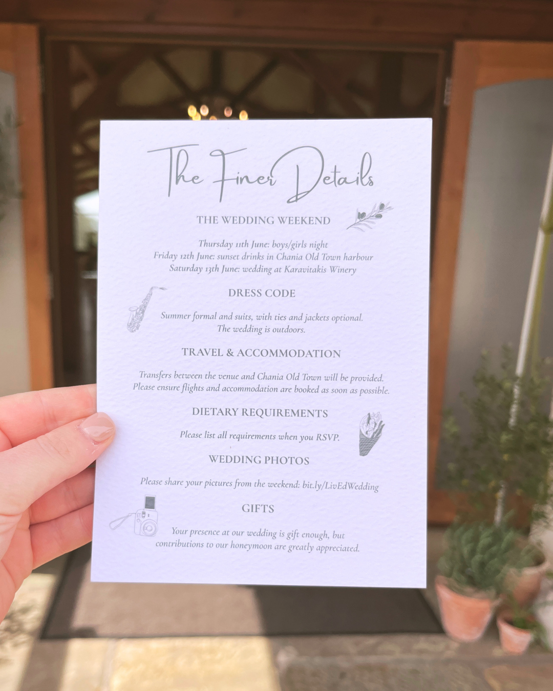 A printed wedding weekend itinerary with details about dress code, travel, accommodations, dietary requirements, wedding photos, and gifts, held outdoors at a location with a wooden entrance and potted plants nearby.