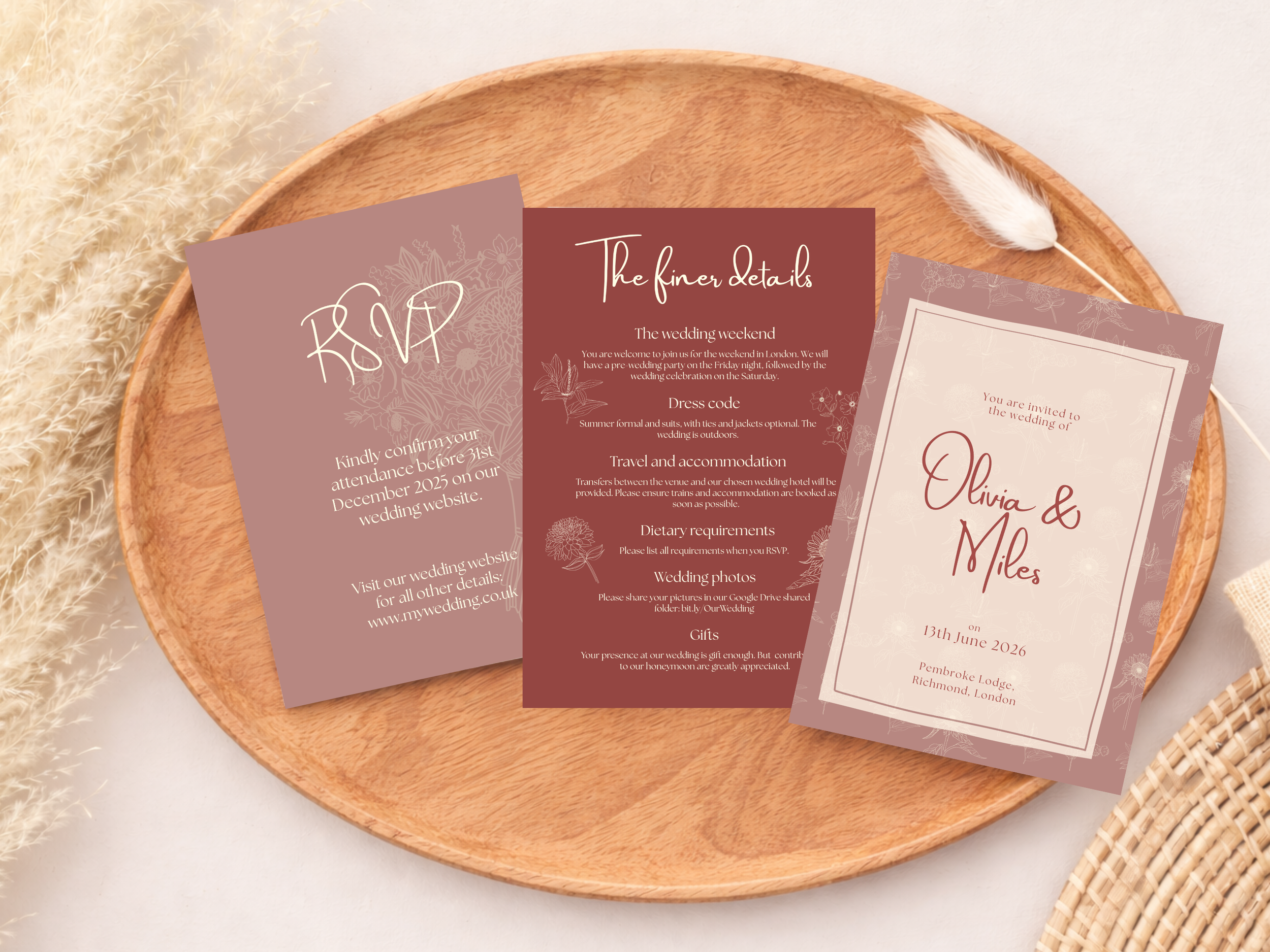 Wedding invitation cards placed on a round wooden tray with a white fluffy plant on the left and a small woven basket on the right.