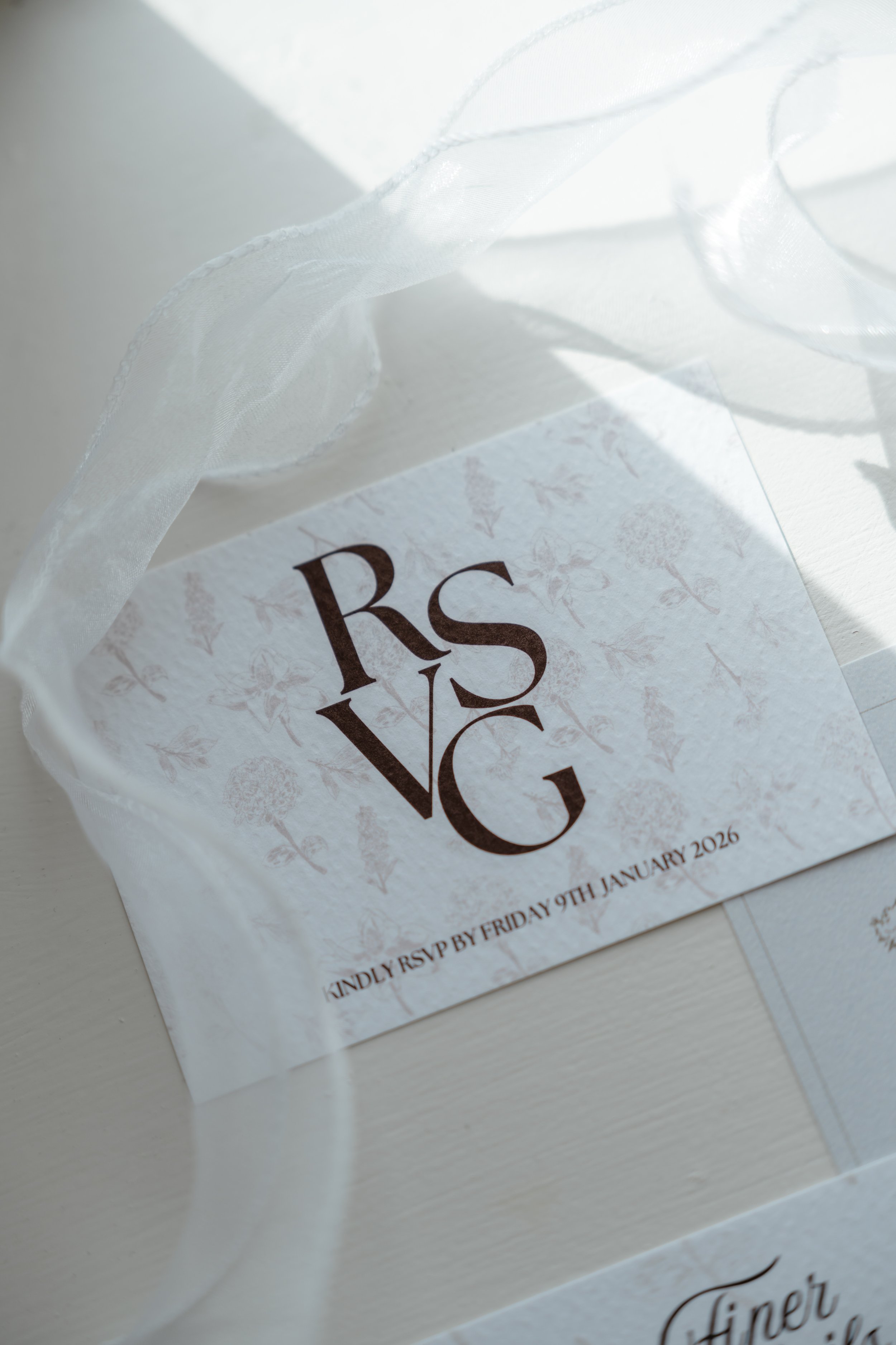 Close-up of wedding invitation card with elegant white ribbon. Text on the card reads 