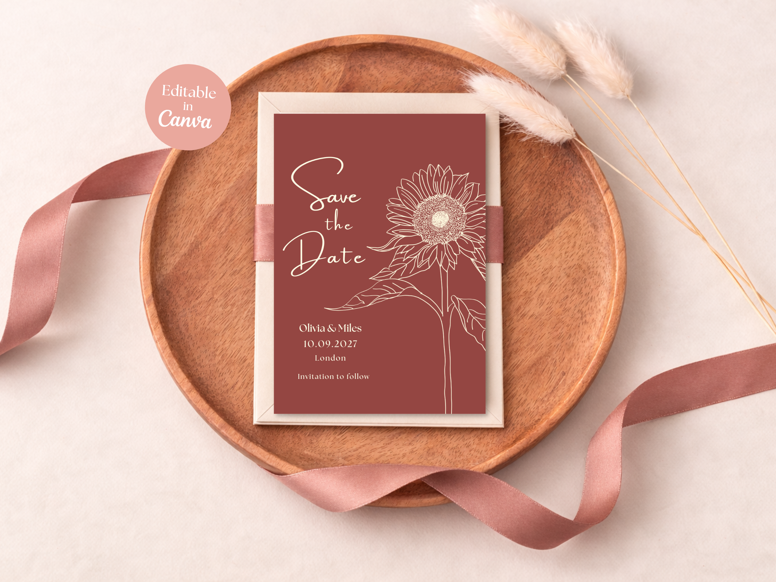 A wedding save the date card with a line drawing of a sunflower, placed on a white background inside a wooden tray, accompanied by a pink ribbon and dried flowers.