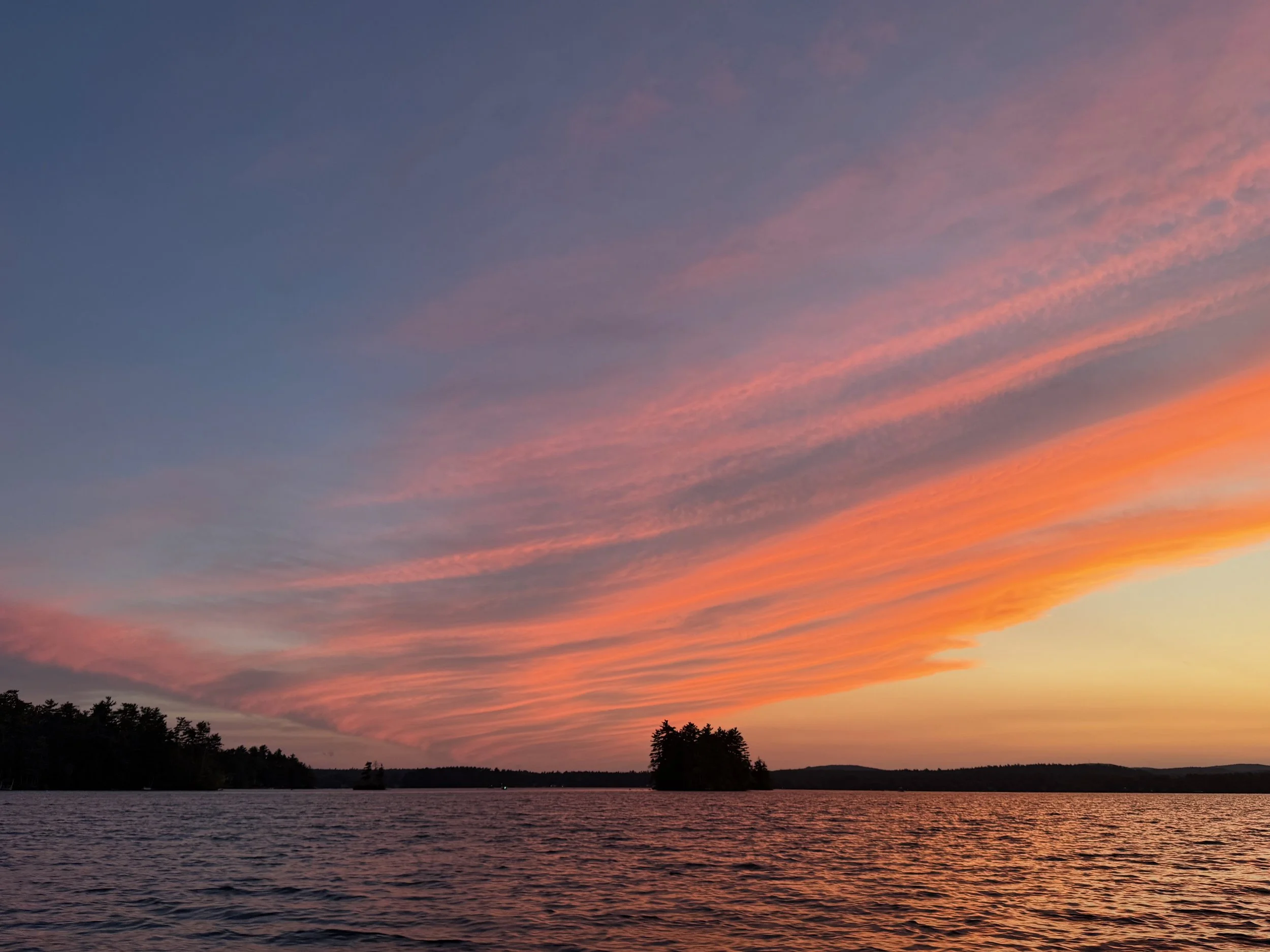 Scenic view of a sunset over a lake with colorful sky and silhouettes of trees at the horizon.