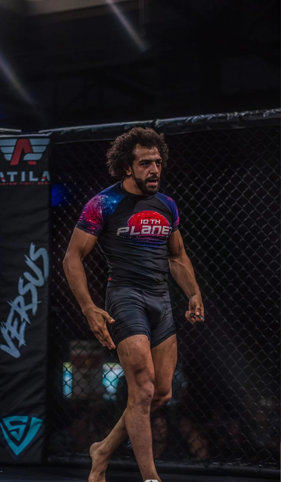 A male mixed martial arts fighter in a cage, wearing training shorts and a shirt with the logo "10TH PLANE".