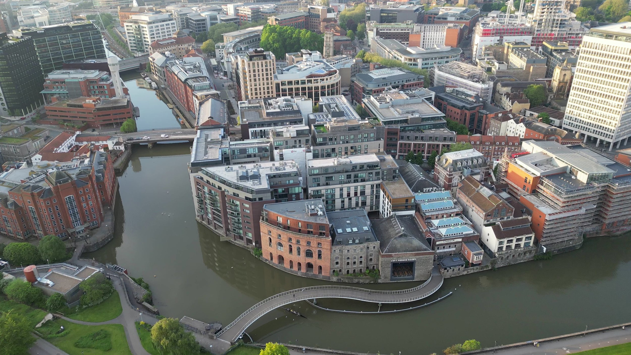 Aerial view of a city skyline with a river running through it, showing various modern and historic buildings, bridges, and green spaces.
