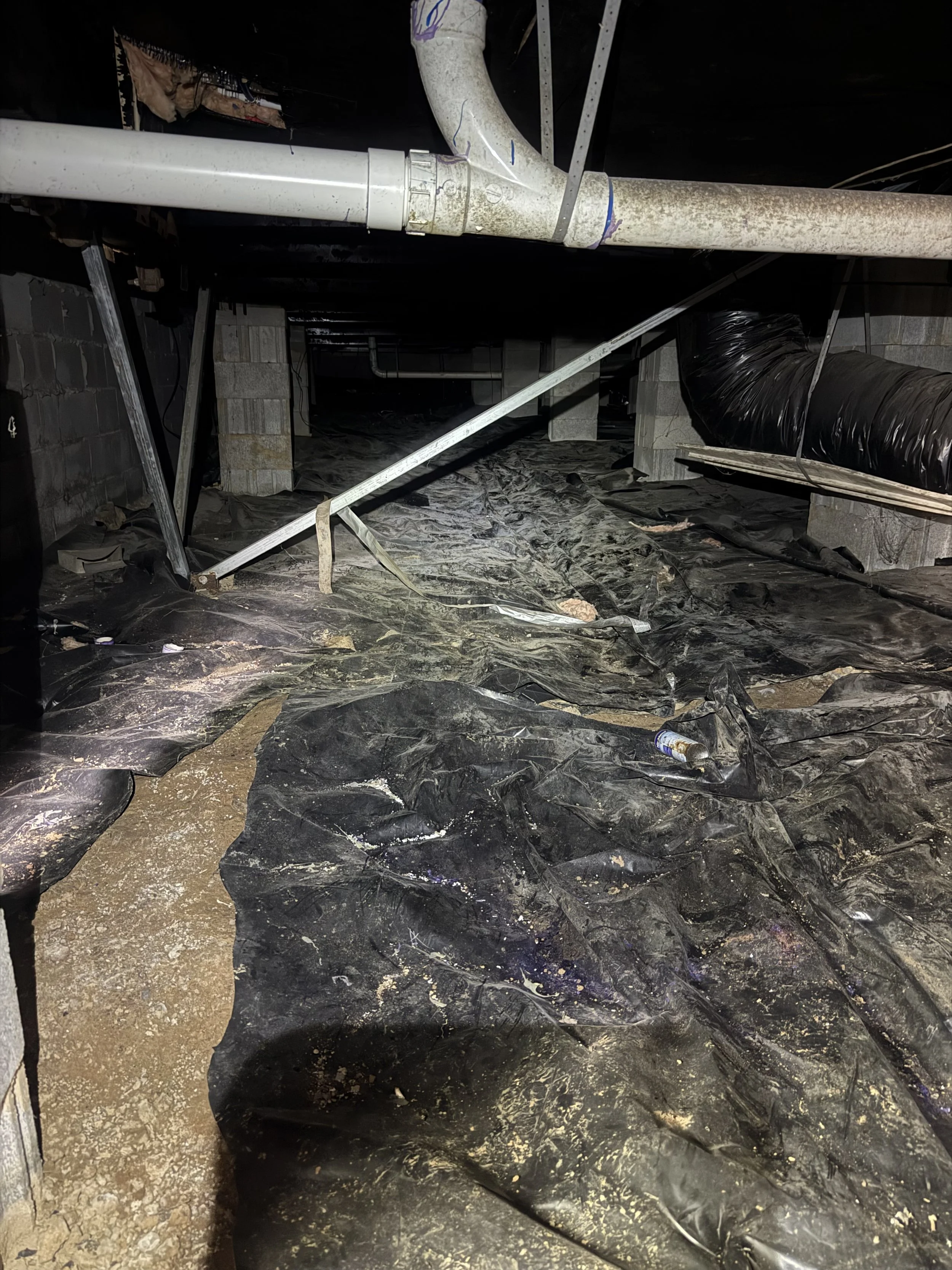 Construction or renovation site showing pipes, black plastic sheeting on the floor, and concrete blocks supporting the structure.