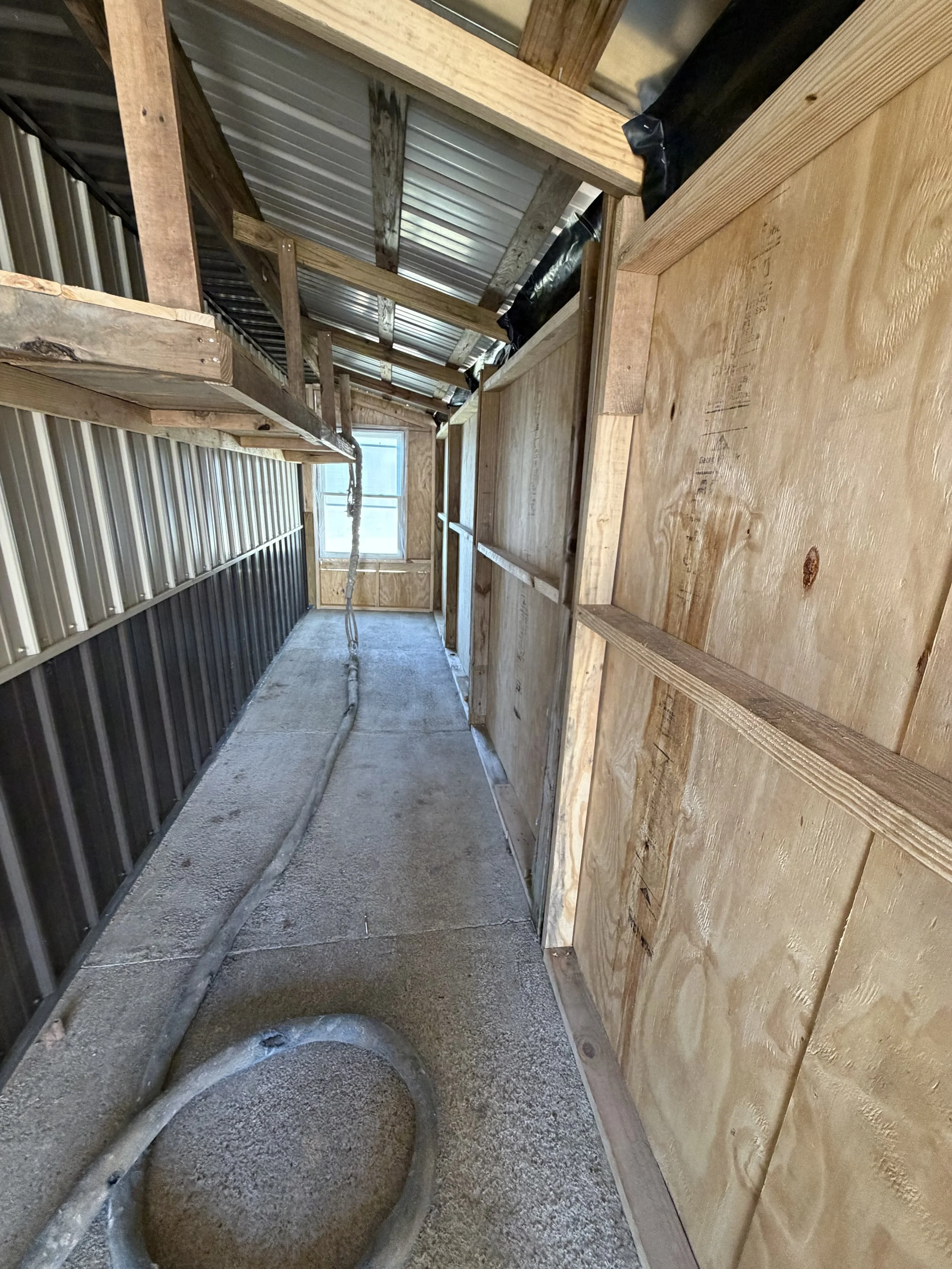 Interior of a partially constructed building with wooden framing, a small window at the end, and a coiled cable on the concrete floor.