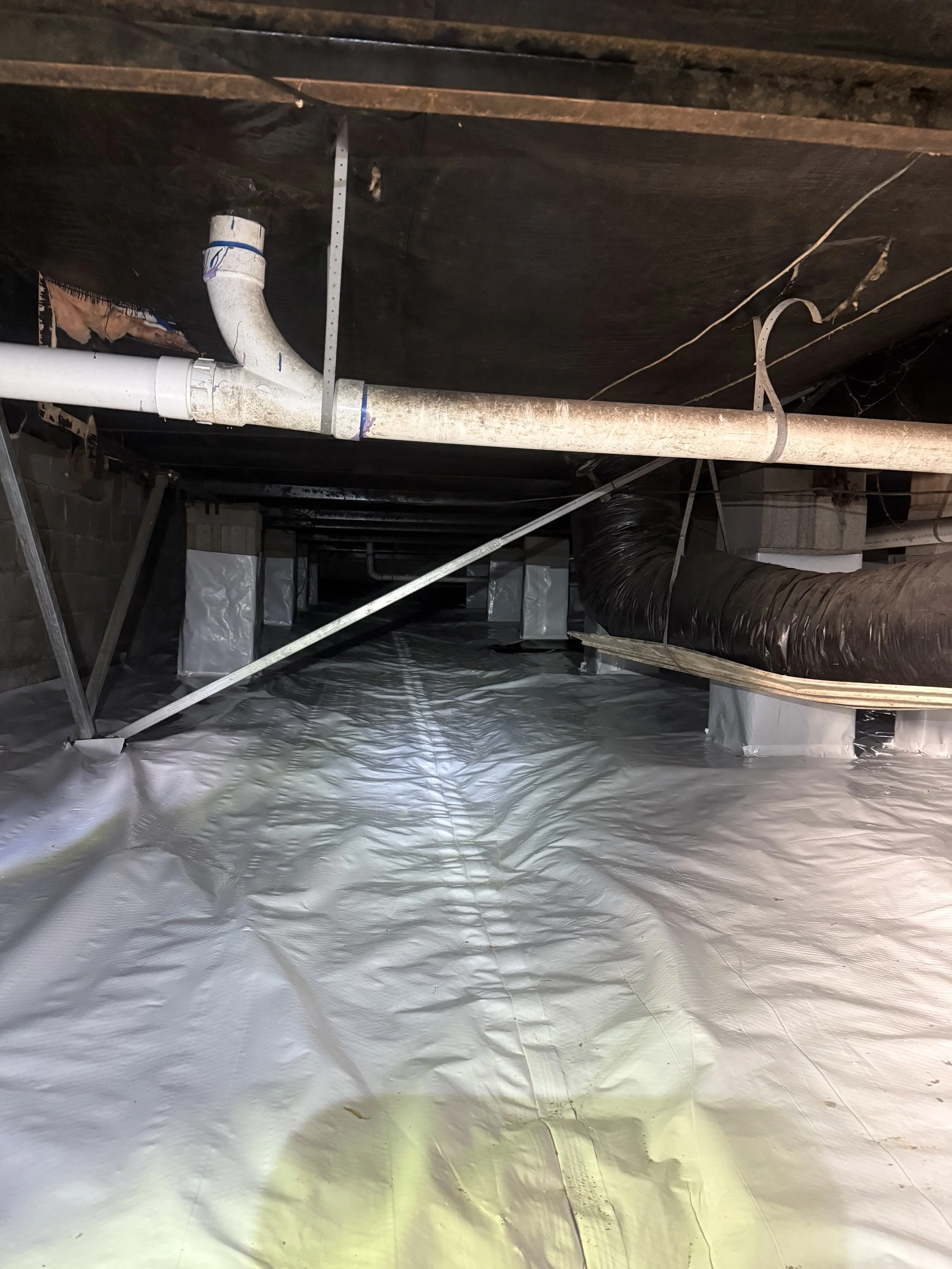 View of a crawl space with white vapor barrier, exposed pipes, and ductwork.