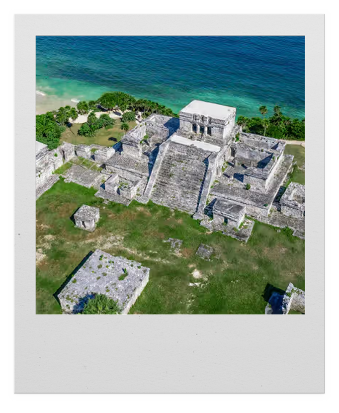 Aerial view of ancient stone ruins near the ocean, surrounded by green grass and trees.