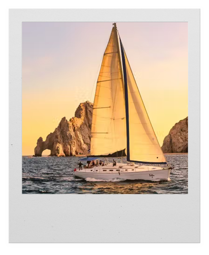 A sailboat with yellow sails on the water near rocky islands at sunset.