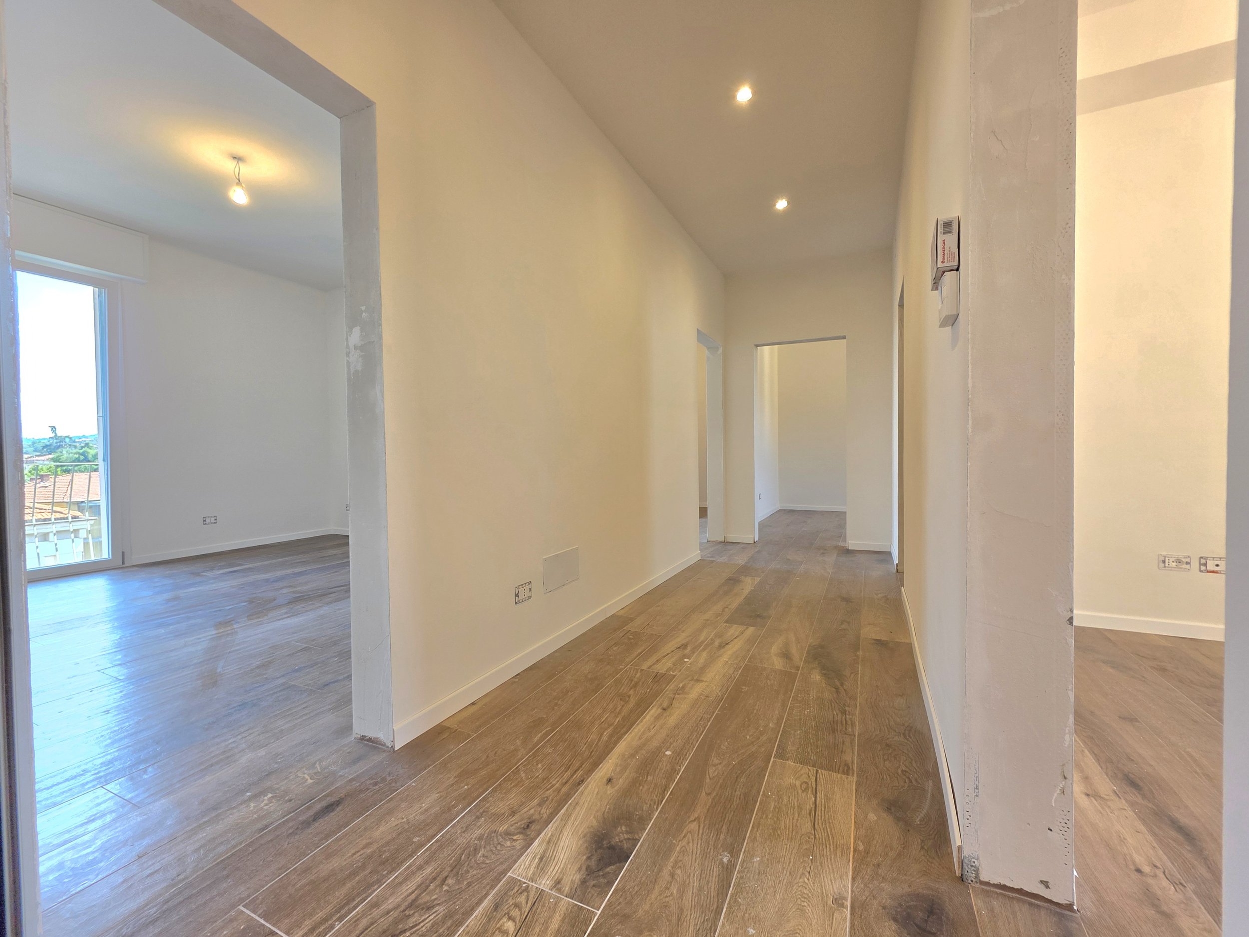 Interno di un appartamento non arredato con pareti bianche e pavimento in legno, in fase di ristrutturazione, con aperture verso altre stanze