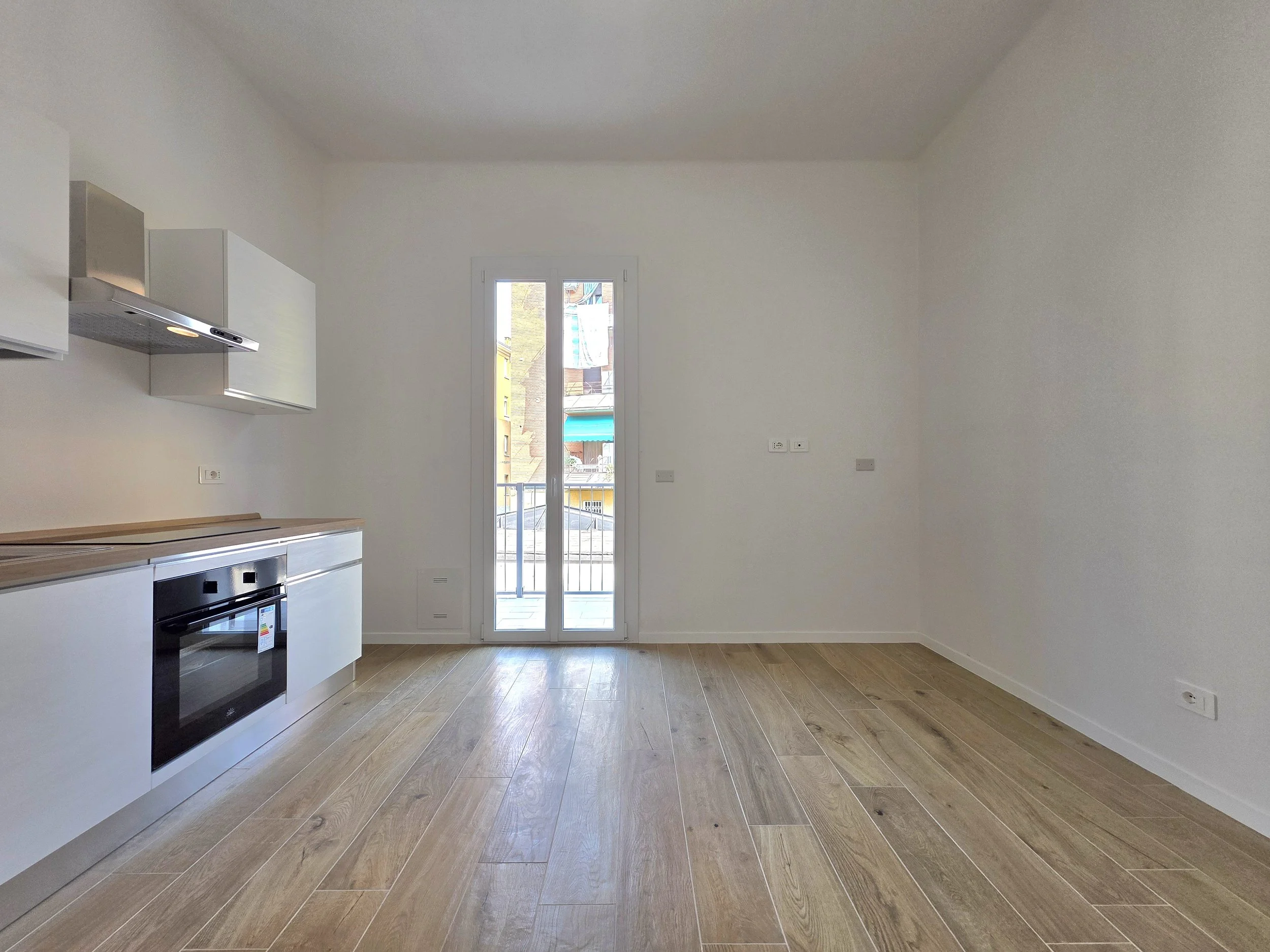 Cucina vuota con balcone, pareti bianche e pavimento in legno