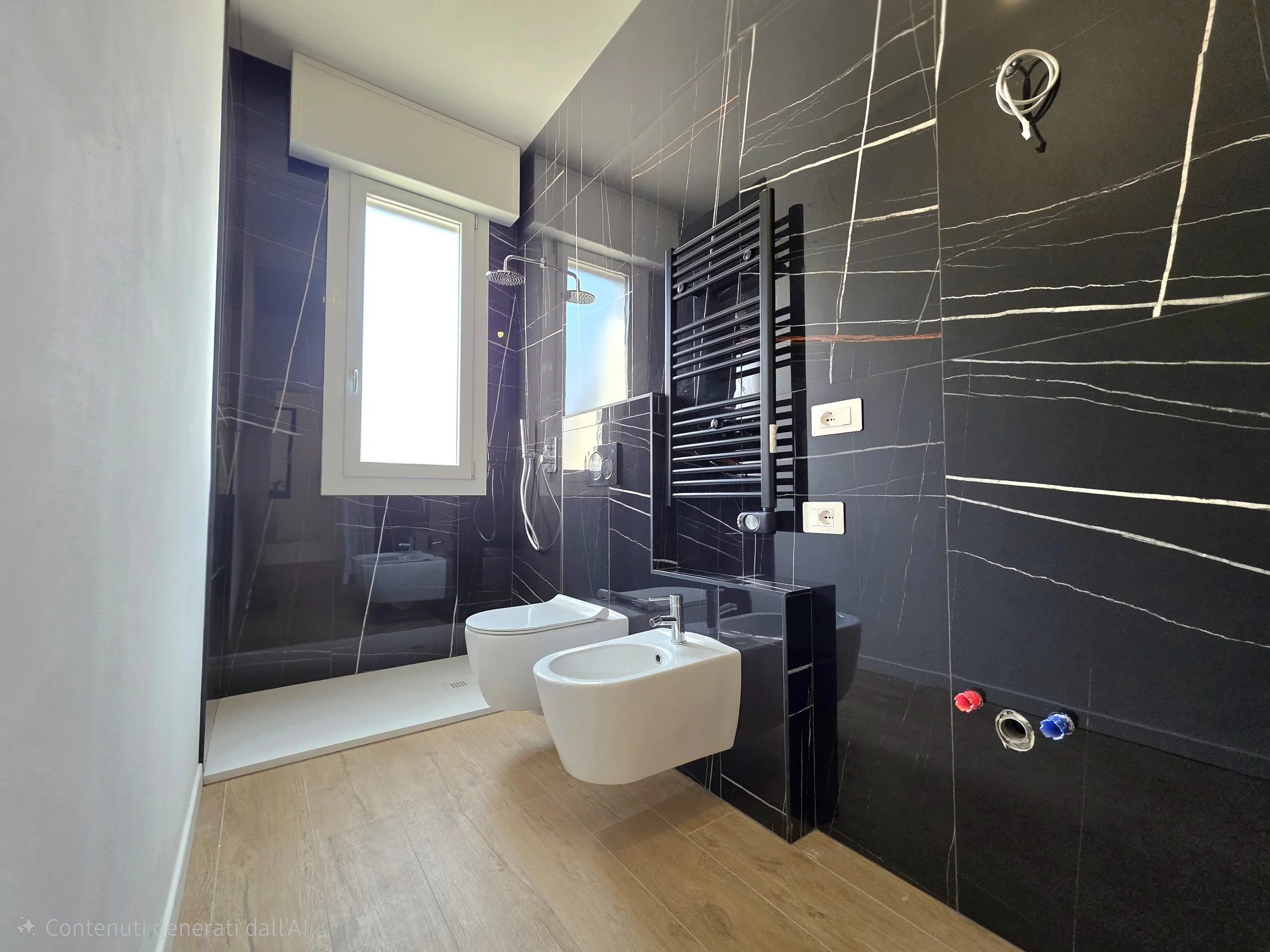 Bagno moderno con pareti e pavimenti in marmo nero con venature bianche. Sono presenti un vaso sanitario e un bidet, un radiatore a piastrelle nere, una finestra e un soffione a pioggia.