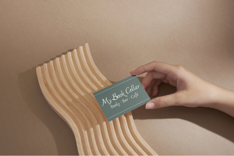 A person holding a teal business card that reads "My Book Cellar, Book's Bar, Cafe"