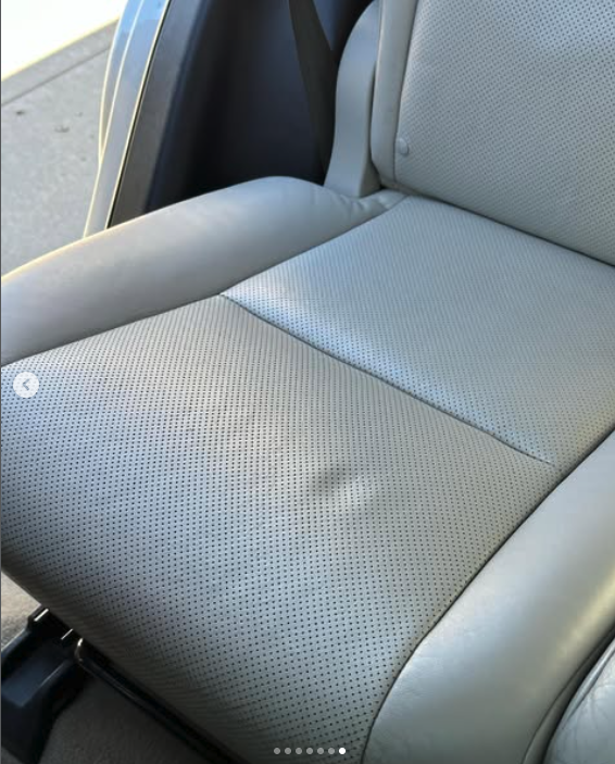 Car seat with light gray leather upholstery and perforated fabric, showing a worn and wrinkled area.