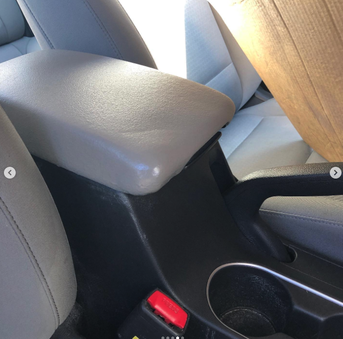 View of the center console between front seats in a car, showing a beige armrest, a red emergency brake button, and a cup holder.