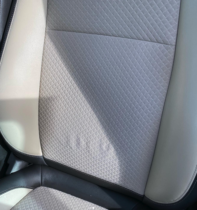 Close-up of a car seat with a light gray quilted fabric center and beige side panels.